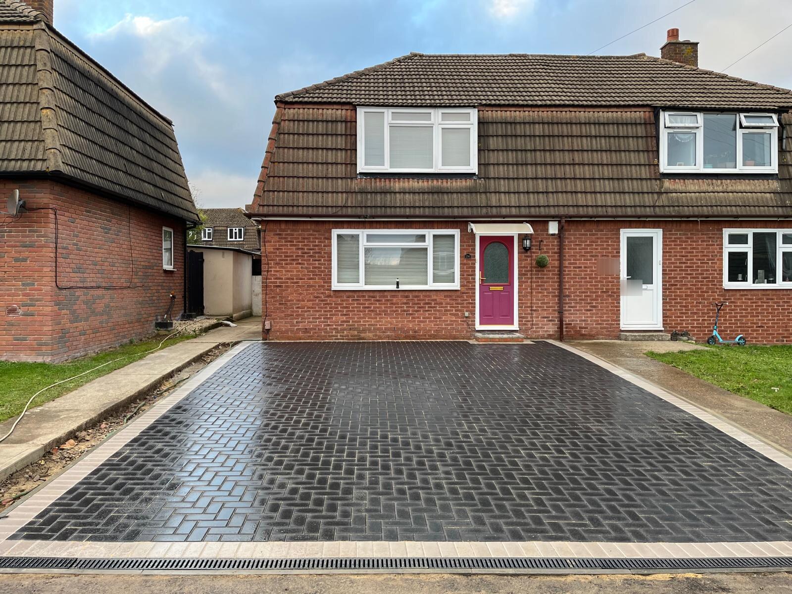 Black herringbone block paving driveway in Bexley with a grey border and channel drain across the entrance