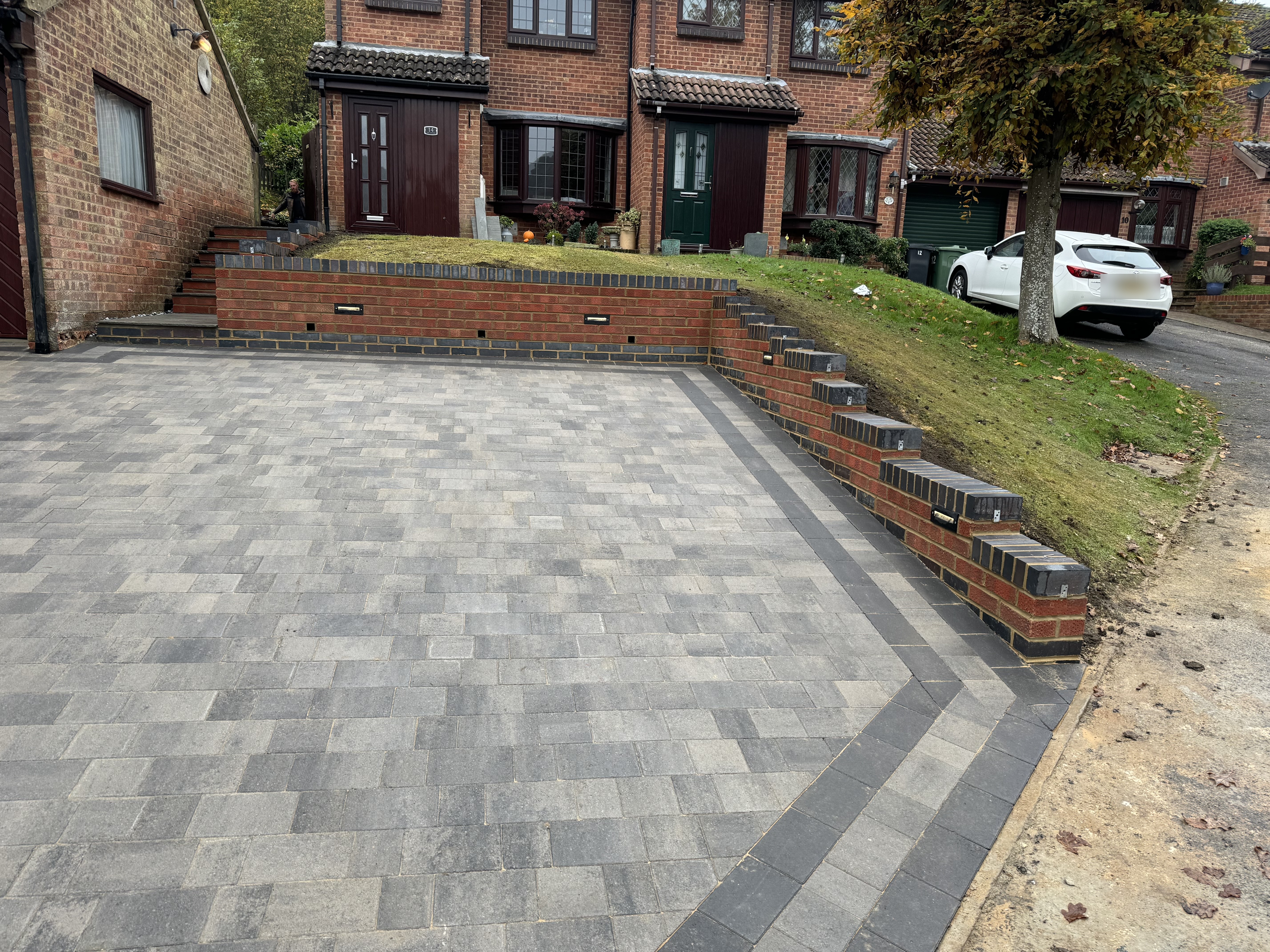 A newly completed block-paved driveway with contrasting border, brick retaining walls, and integrated step lighting