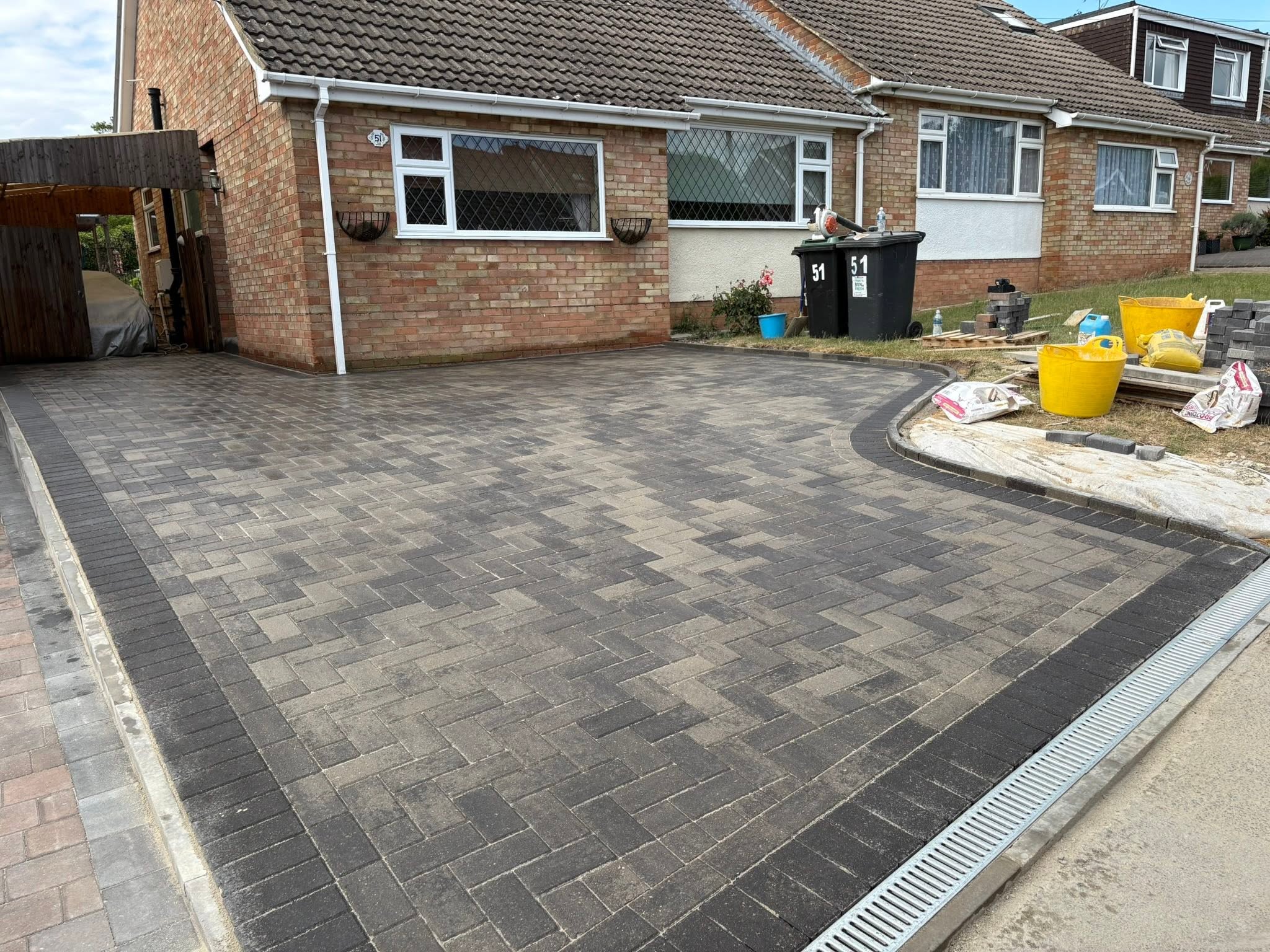 Close view of Brett Trio Burnt Oak block paving with charcoal border and ACO drain in front of a bungalow in Burham, Medway