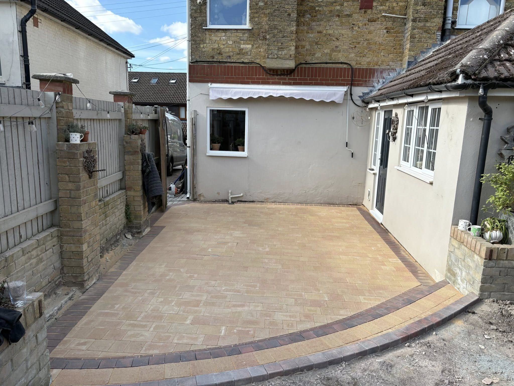 Wide angle view of finished mellow yellow block paving rear garden with brindle border in Canterbury