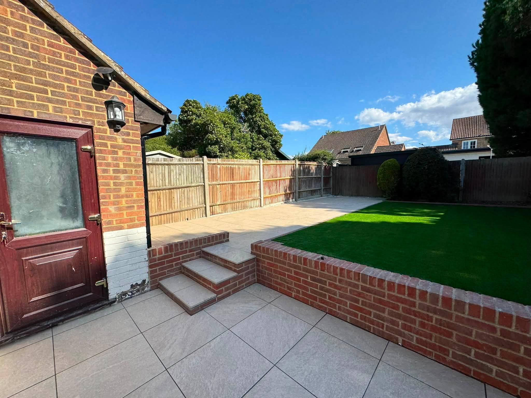 New 9-inch brick retaining wall and steps with Aura Beige porcelain below and artificial grass above in Hempstead