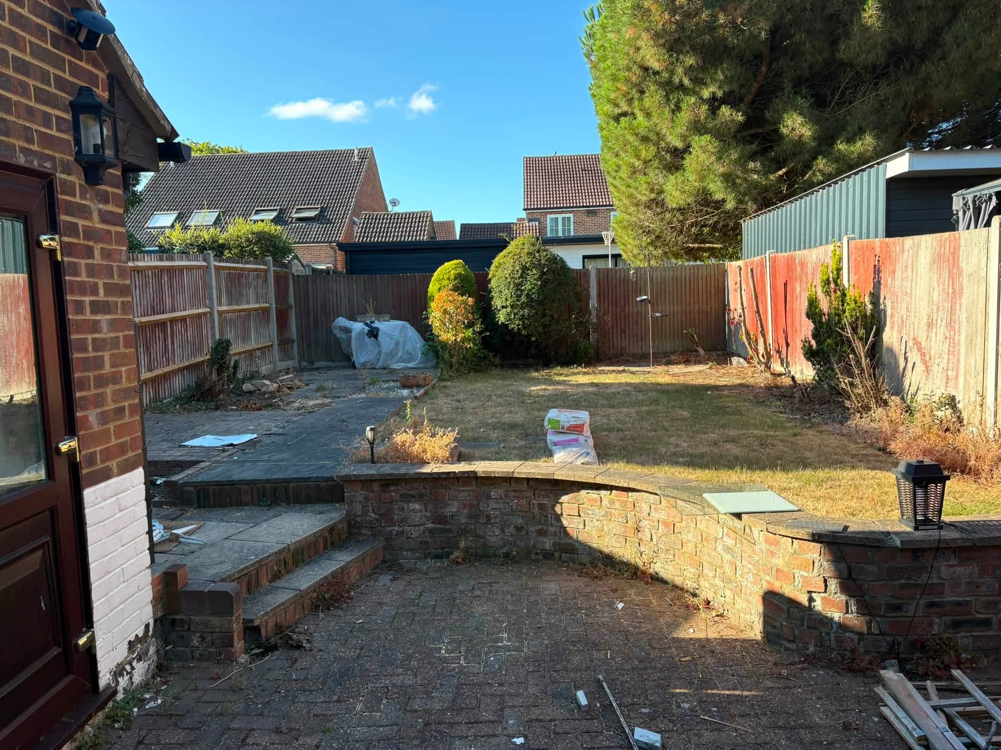 Old curved brick retaining wall, worn block paving and dry lawn in a Hempstead garden before the makeover