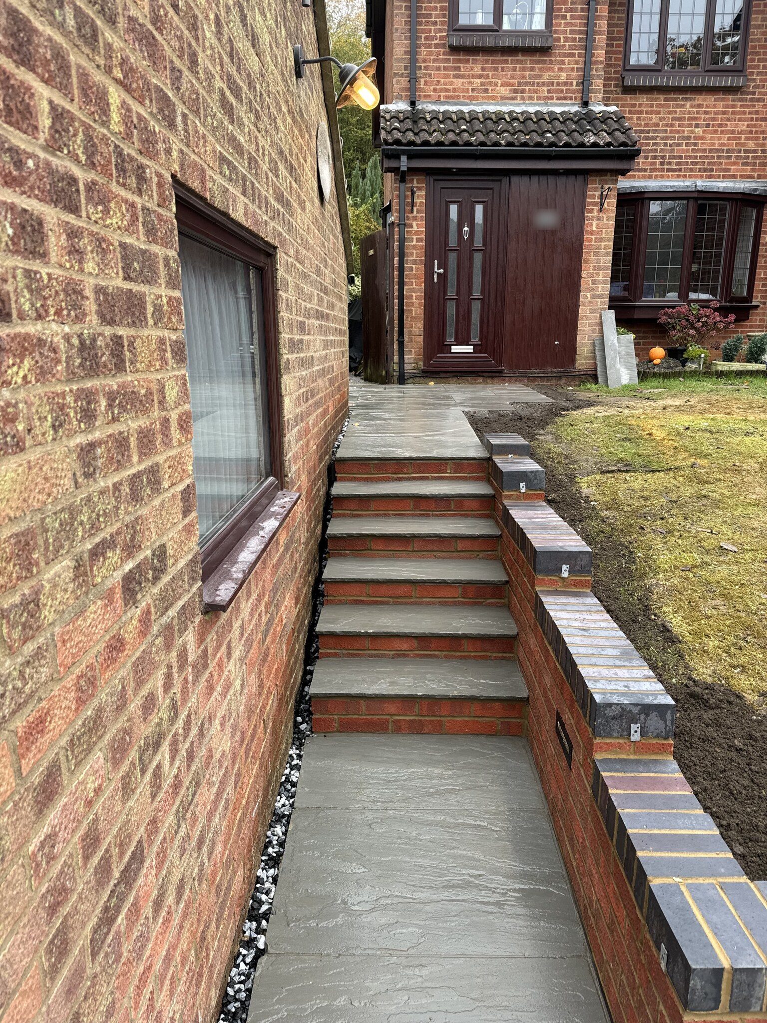 Stone steps and a brick retaining wall with blue brick coping leading up from a block paving driveway in Kent