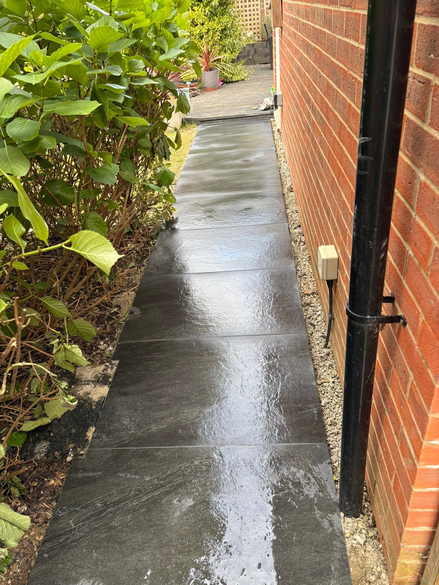 Dark porcelain paving path along the side of a brick house in Maidstone with garden borders