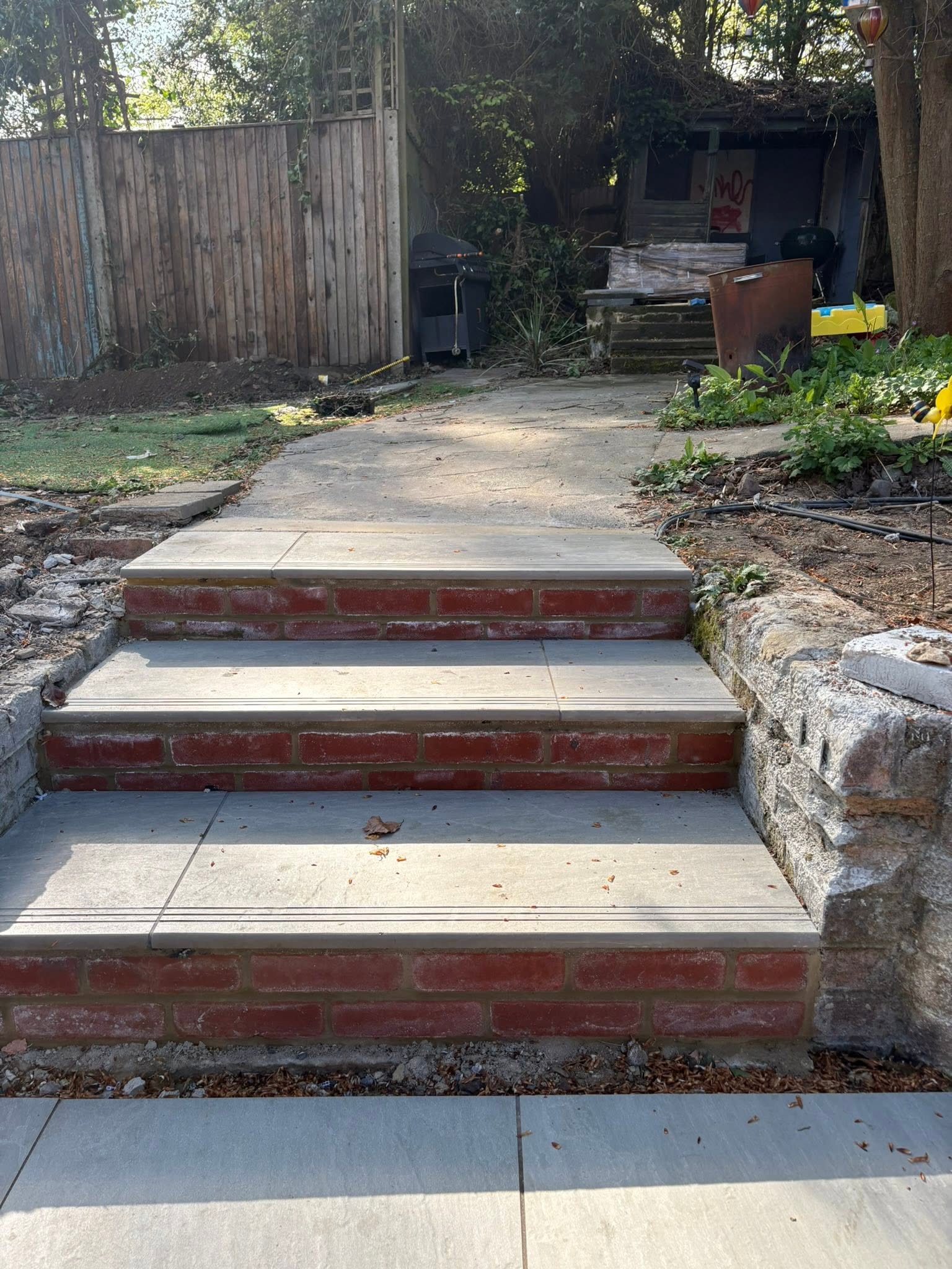 Brick-faced split-level porcelain steps in a Medway garden linking the lower path to the upper Kandla Grey patio