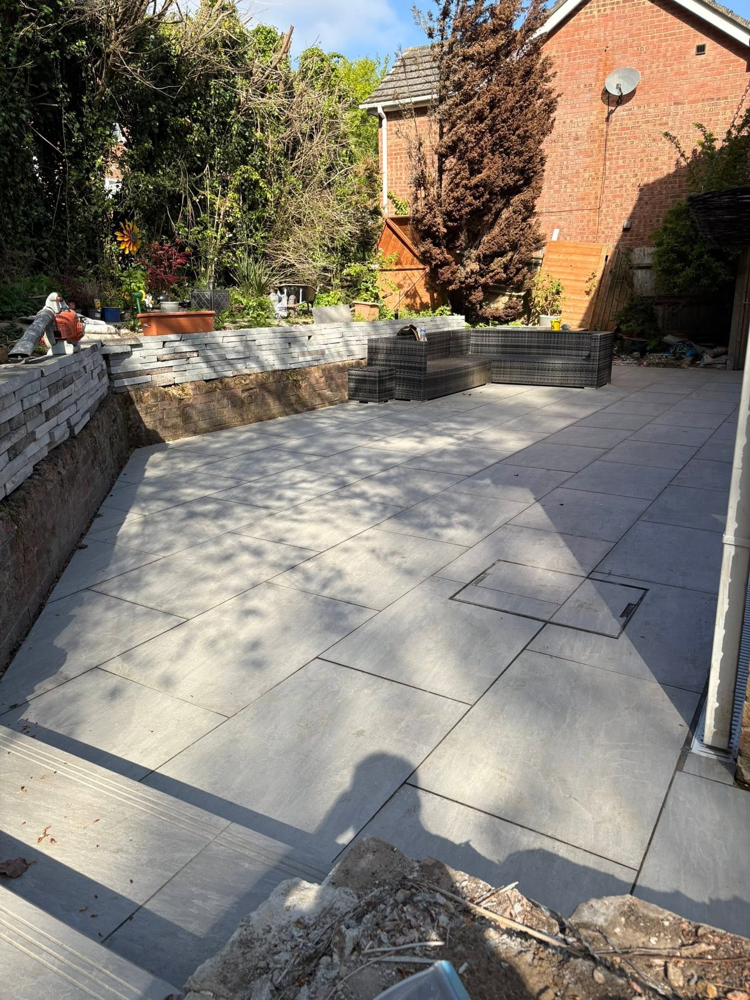 Kandla Grey porcelain patio in Medway with natural stone retaining wall, raised planters and rattan garden furniture