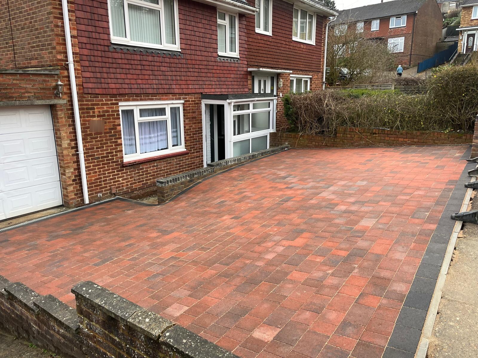 Red block paving driveway with a charcoal border in front of a tile-hung house in Medway