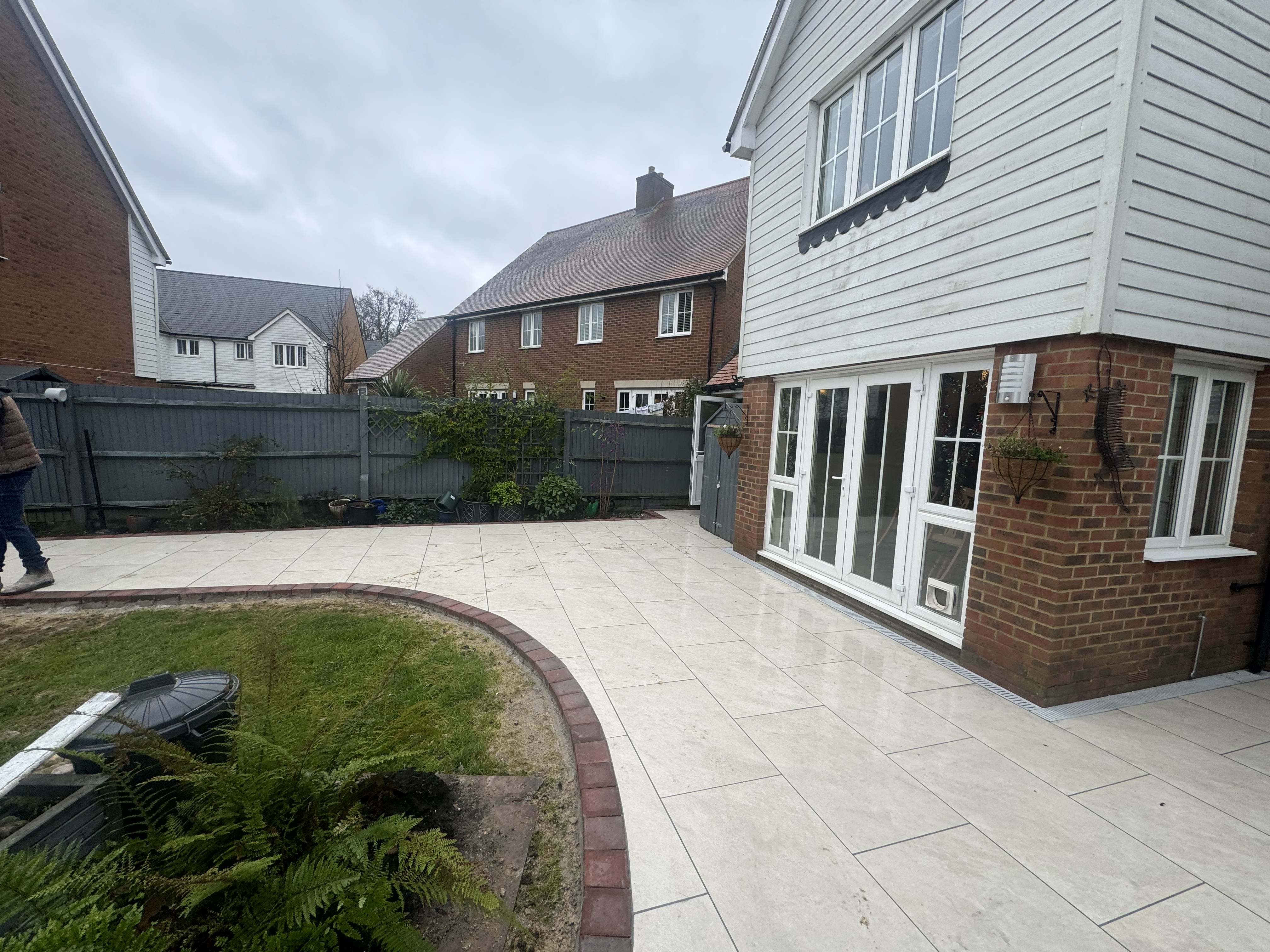 Large-format ivory porcelain patio in Sevenoaks with curved red-brick border and reshaped lawn edge