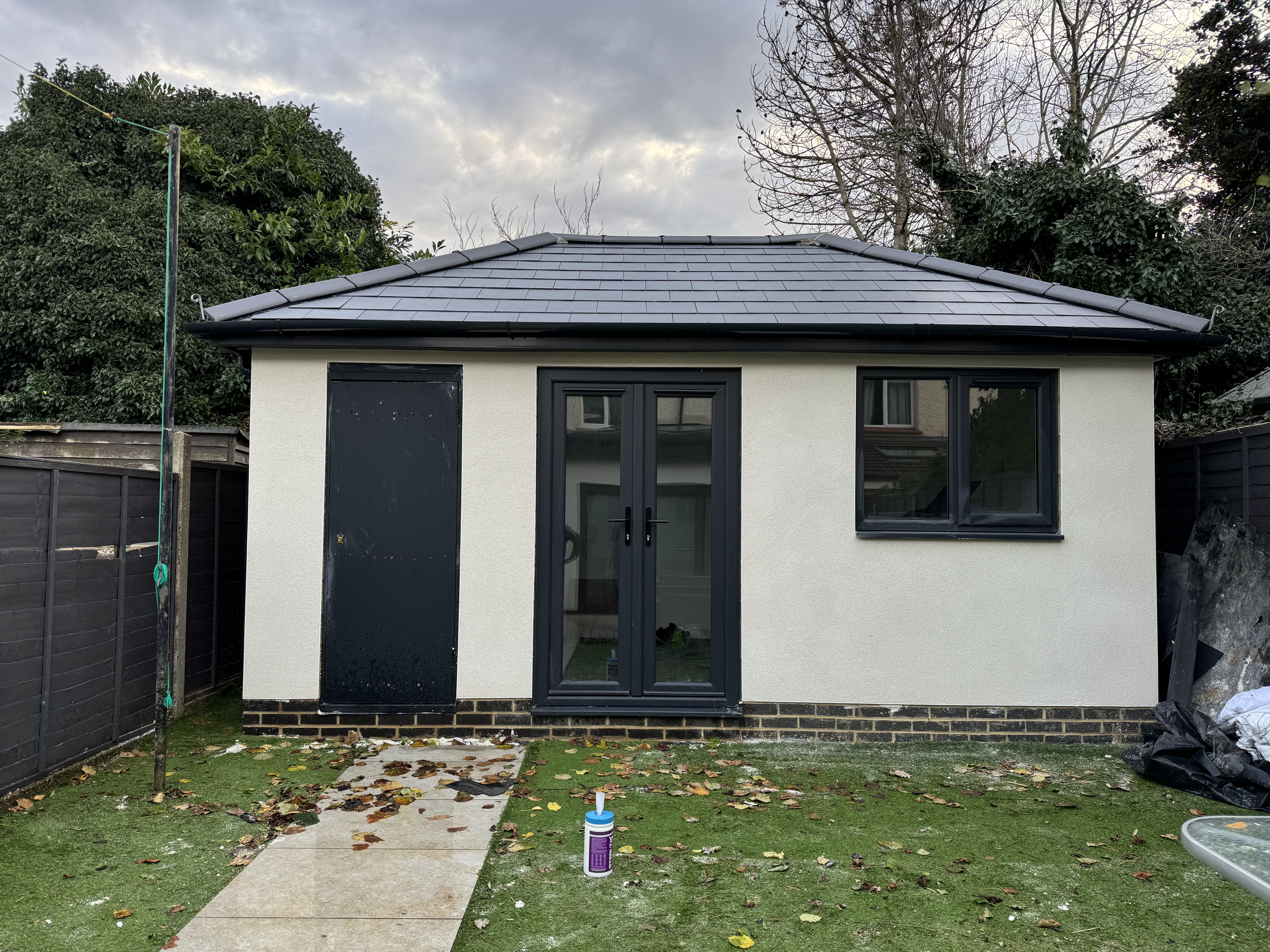 Completed garden outbuilding in Kent with hipped tiled roof, cream render, anthracite French doors and side door