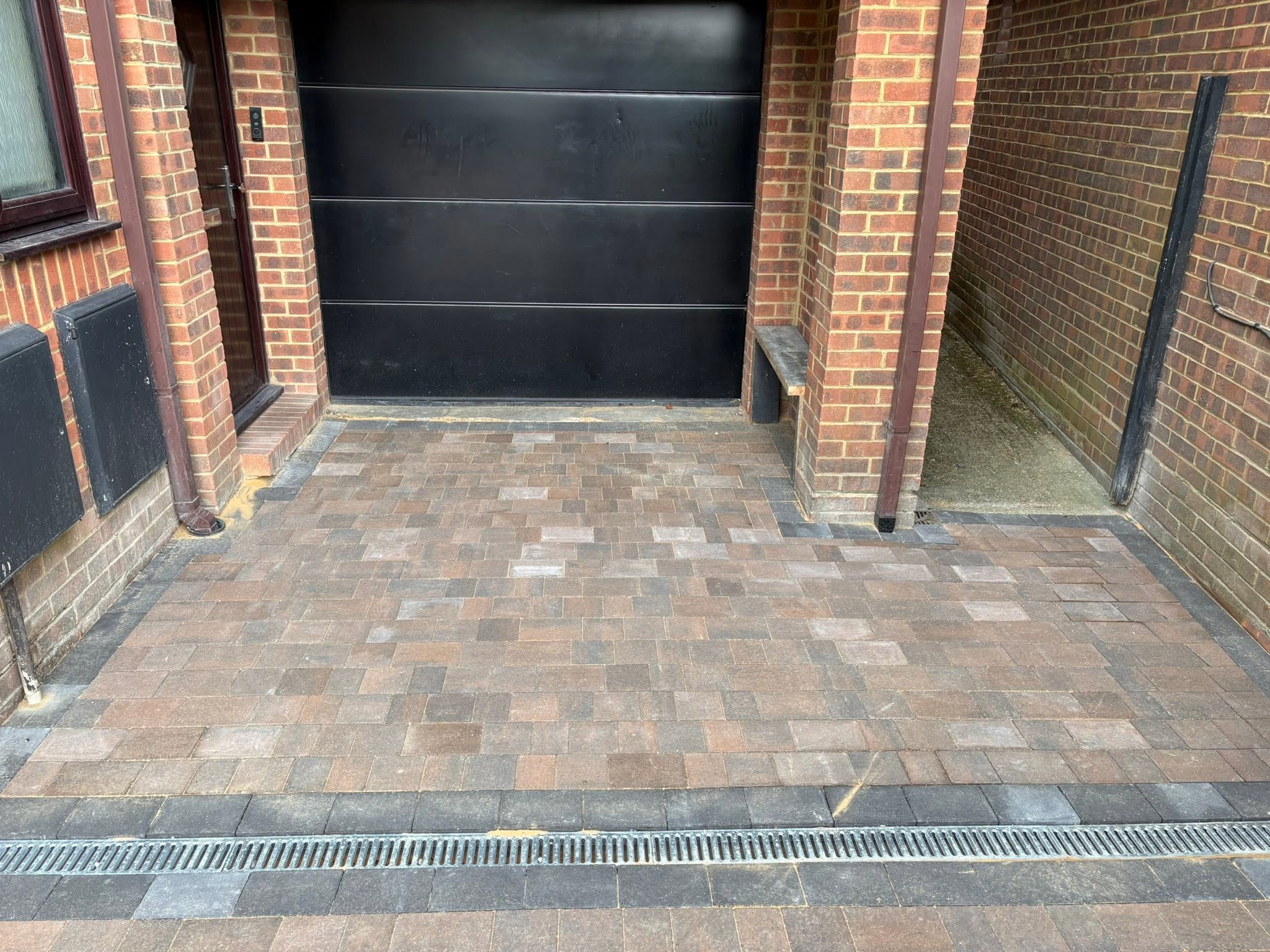 Charcoal border and soldier course detail at the garage threshold with ACO drainage channel on a Sevenoaks block paving driveway